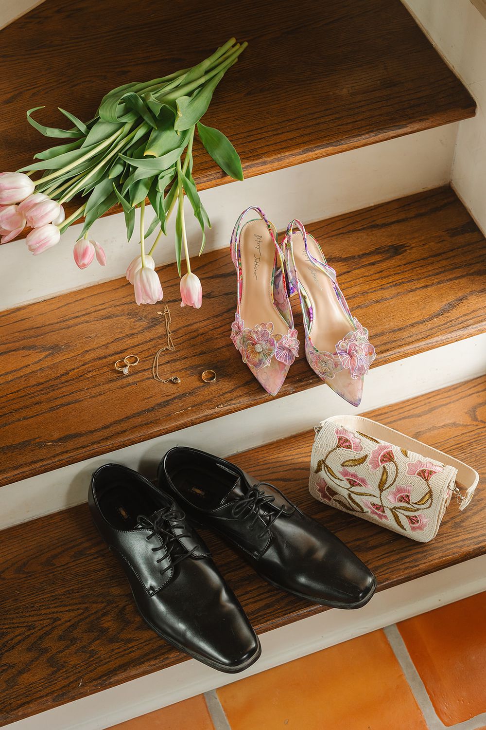 Pink tulips and elegant black formal shoes arranged on wooden stairs in a wedding day preparation setting.