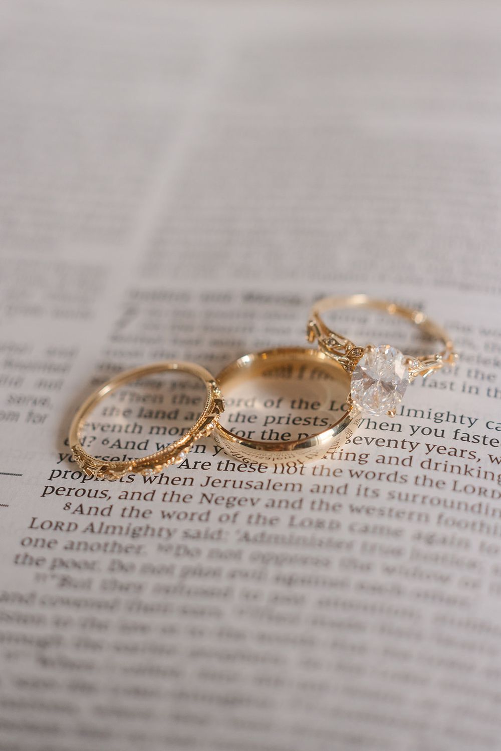 Three golden wedding rings arranged artistically on an open Bible page, with one ring featuring delicate crystal details.