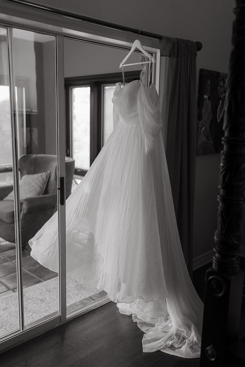 Multiple white wedding dresses hanging against glass windows creating an ethereal black and white display.