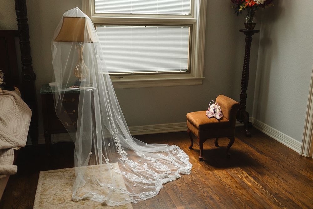 A lace veil trails delicately on a rustic wooden bed against white walls in a sunlit bedroom.