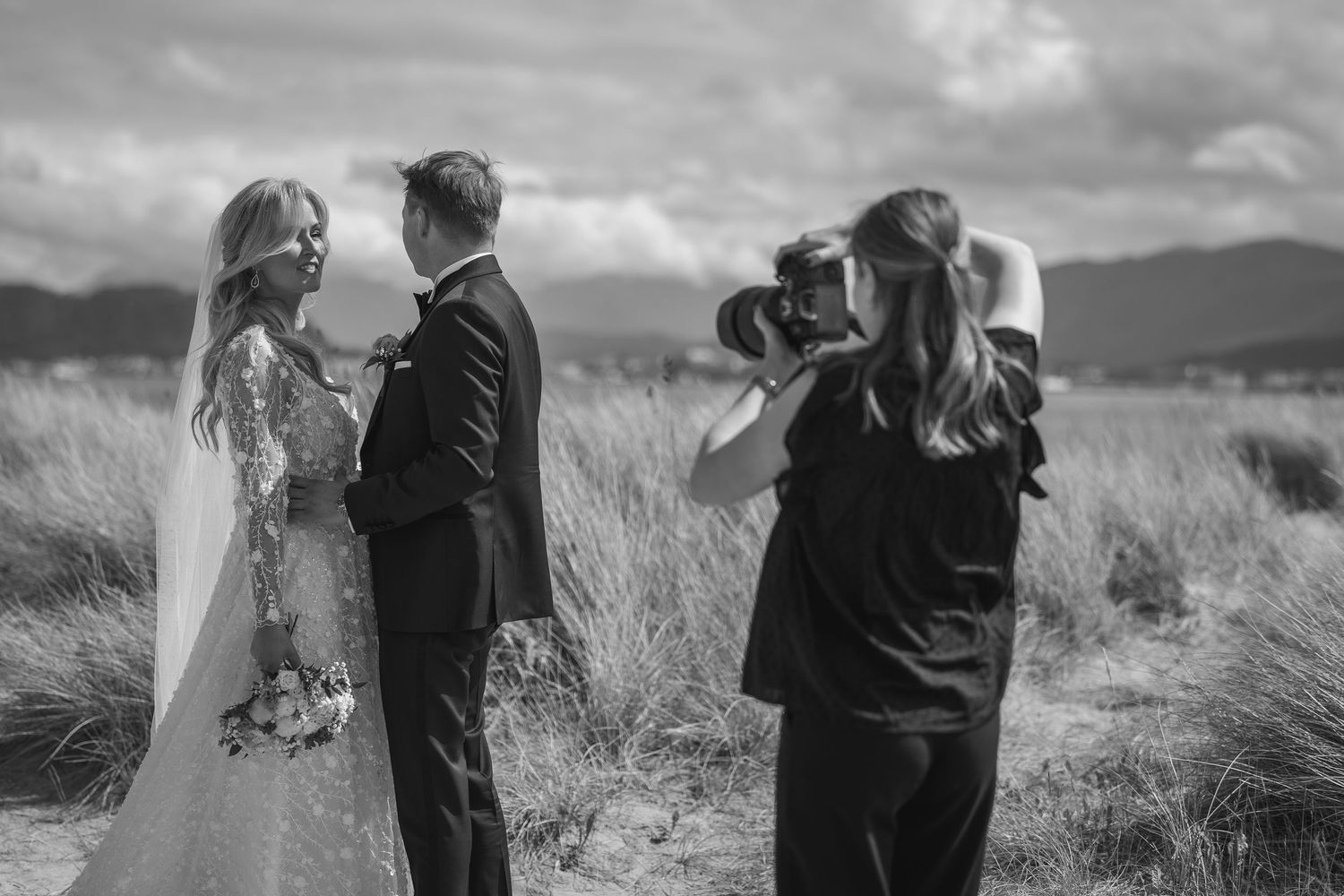 Romantic black and white wedding photos showing couples standing together in a grassy field with mountains in background.