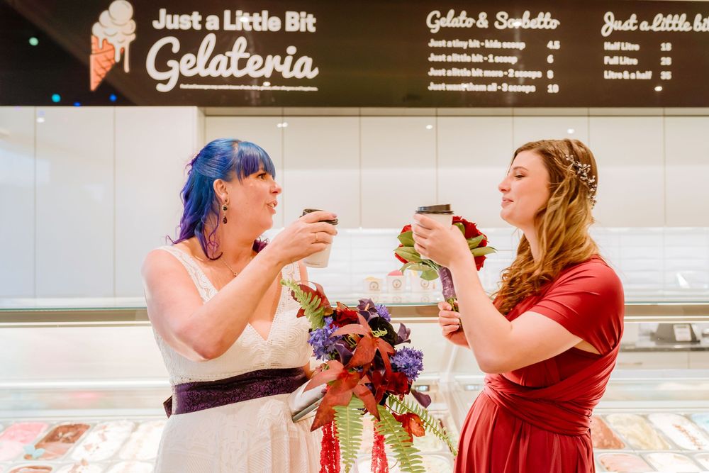 Two people in colorful dresses excitedly share gelato together in front of a gelateria counter.