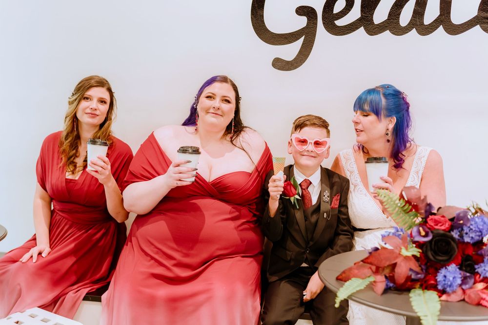 A group dressed in formal attire sits together holding drinks at an elegant event with a gold lettering backdrop.