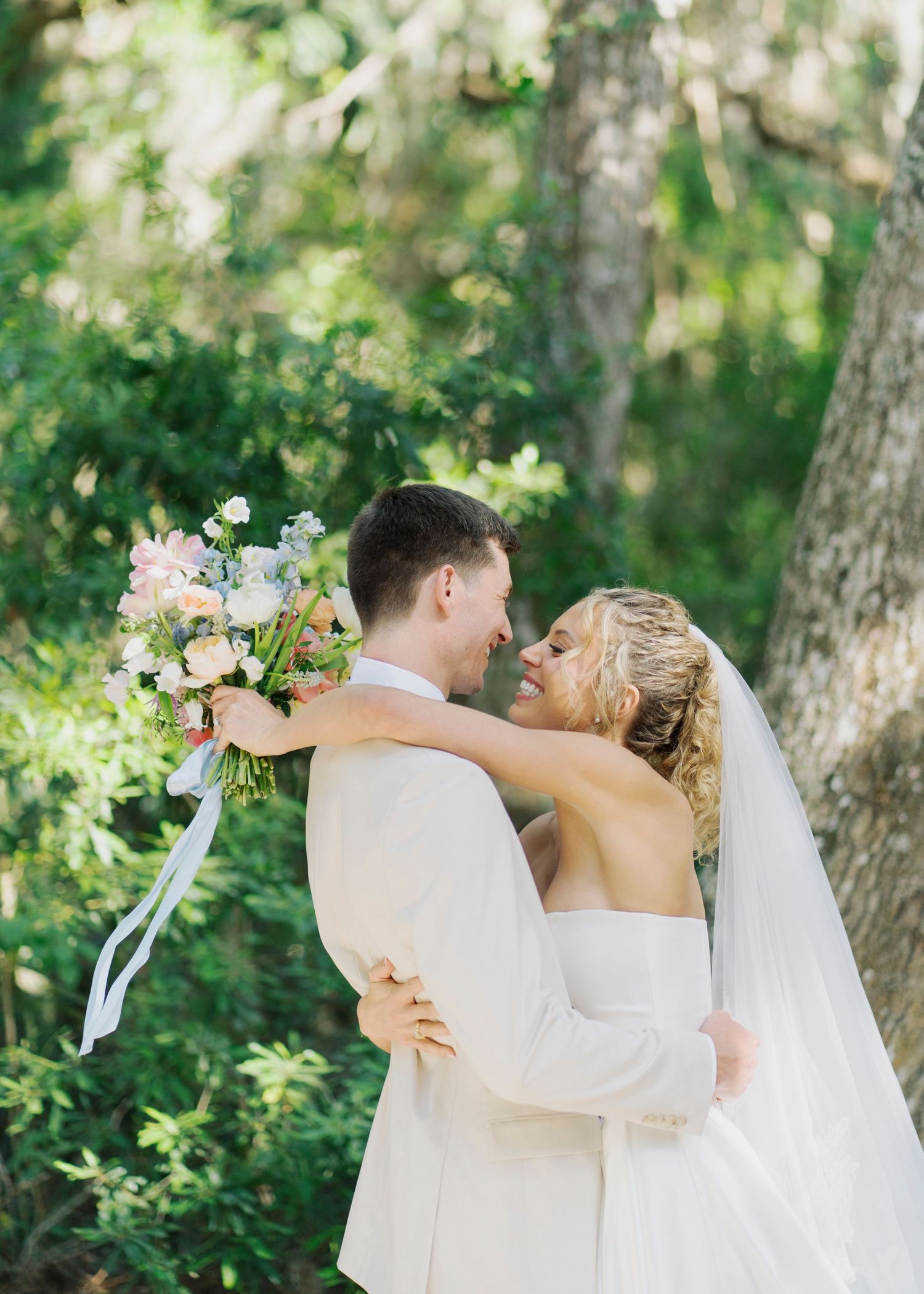 Bride and groom embracing in lush green garden, bride holding elegant blush floral bouquet.