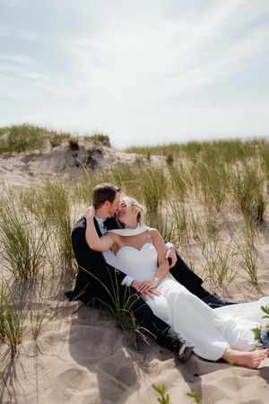 A romantic scene of a couple cuddling in the sand dunes on a beach among tall grass.