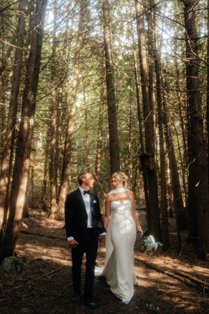 A romantic wedding photoshoot in a sunlit forest with tall trees creating a natural cathedral-like setting.