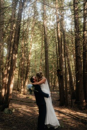 A wedding couple shares intimate moments while walking through a serene wooded area dappled with sunlight.