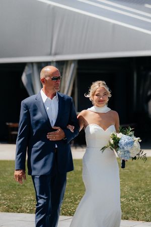 Cheerful wedding couple walking across a sunny lawn in formal white dress and navy suit.