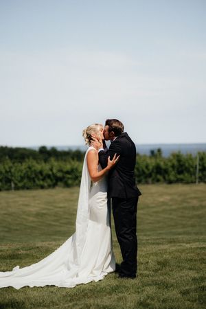 Wedding couple shares an intimate kiss in a scenic outdoor field with mountains and forest in the background.