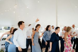 Wedding guests dance and celebrate together under twinkling lights in a white tent reception venue.