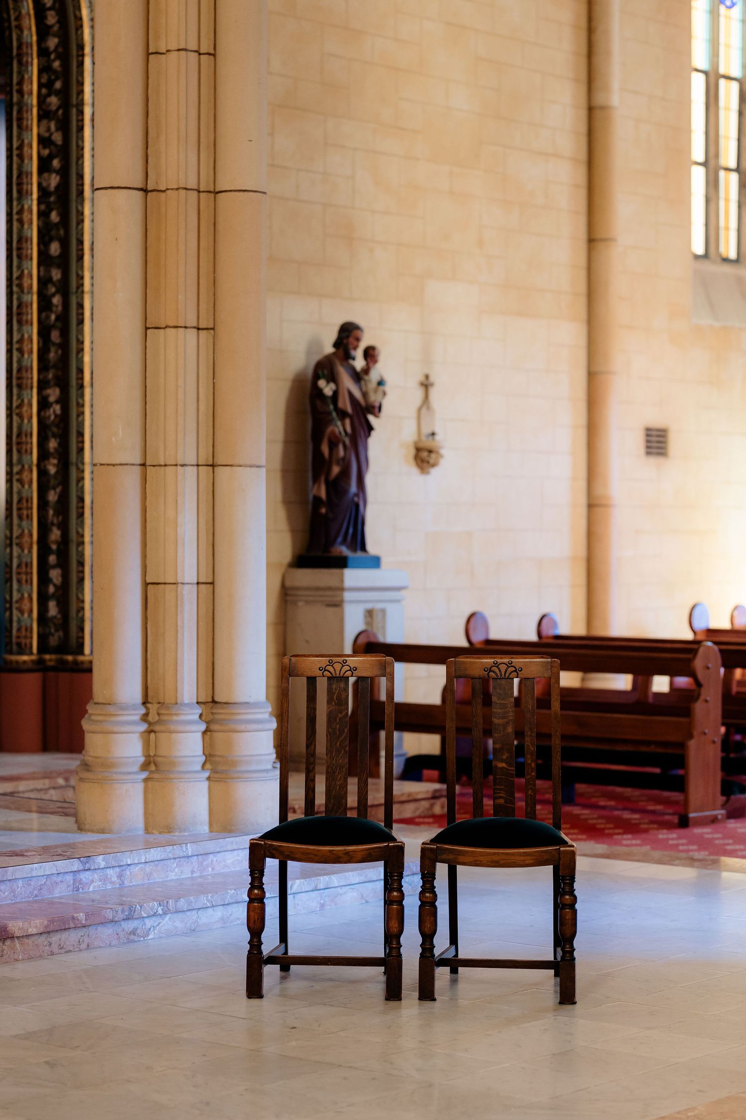 Elegant wooden church pews line the walls of a bright stone interior with high ceilings and ornate architectural details.