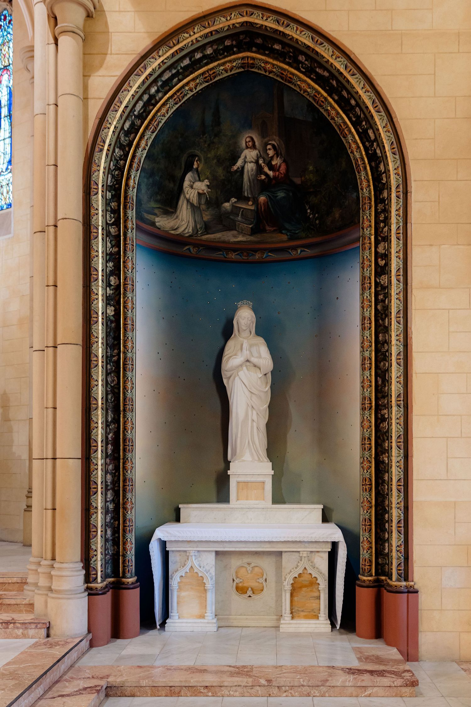 Four stone alcoves in a church with white marble statues and religious ornate archways decorated with gilded details and murals.