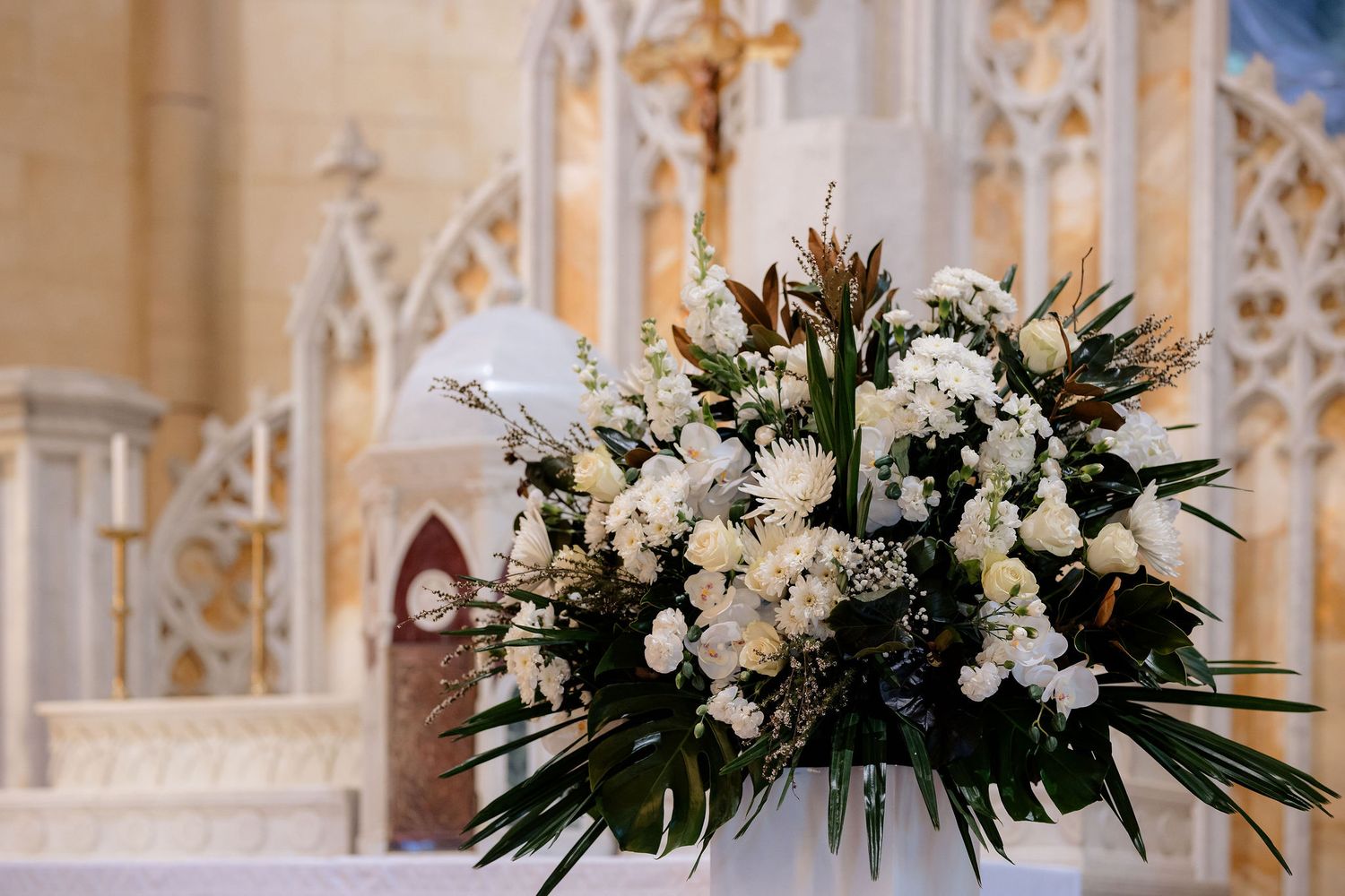 A stunning white floral arrangement with greenery sits atop an altar in an ornate church setting.