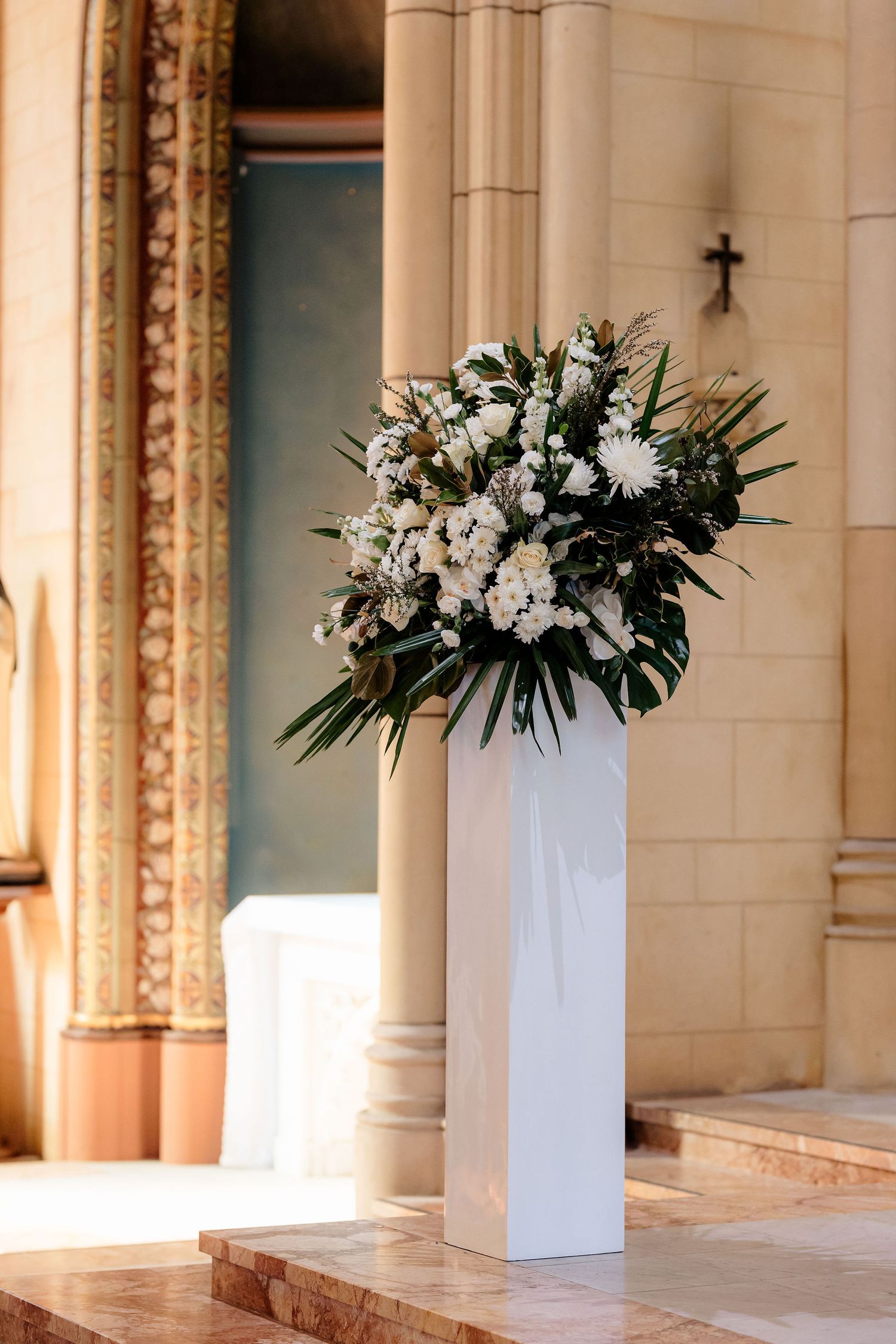 Three elegant white floral arrangements in tall vases sit along a hallway with classical architectural details.