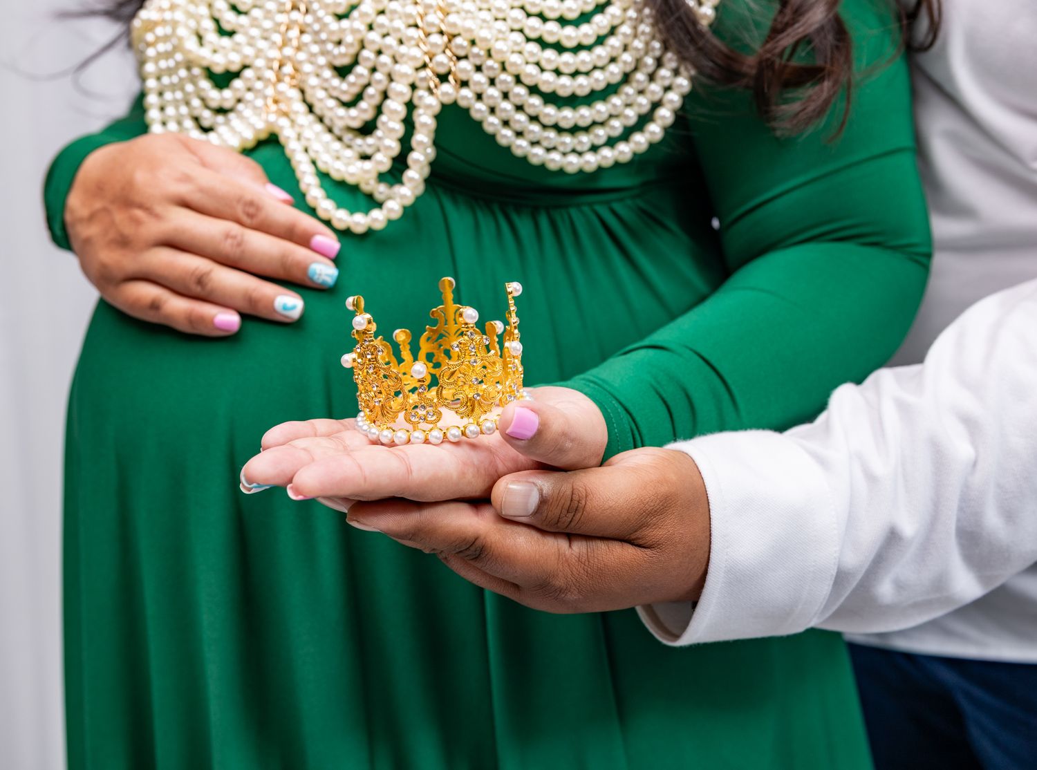 Studio portrait of an expectant mother in a flowing burnt orange gown with bell sleeves and decorative crown headpiece.