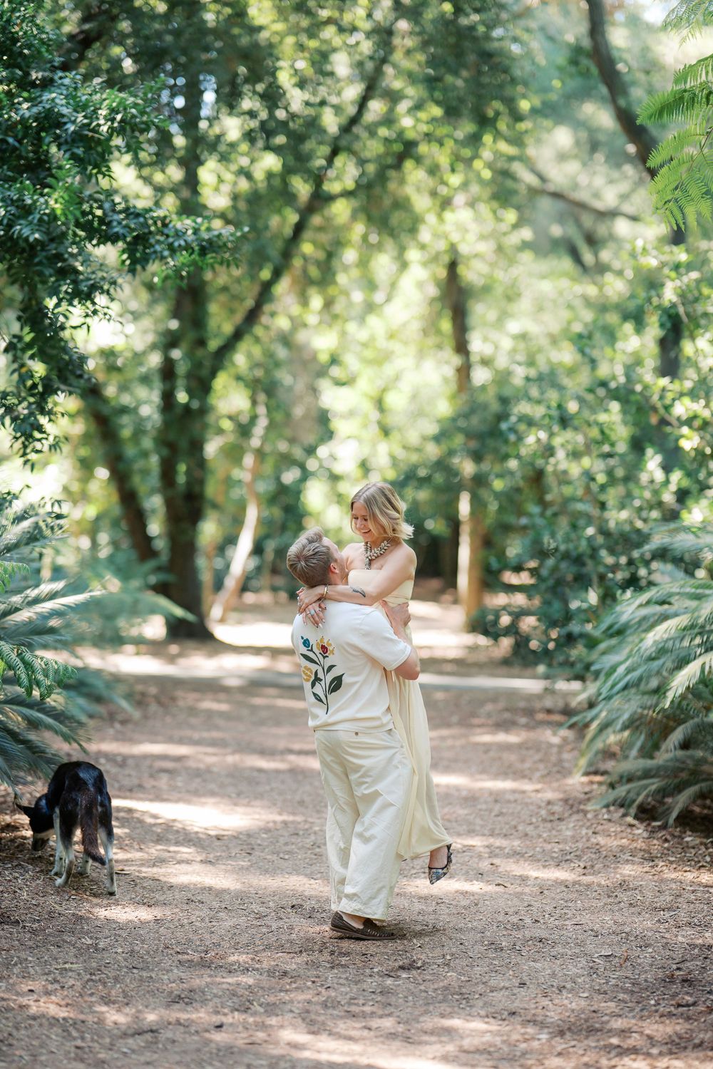 A joyful celebration embrace on a sunlit forest trail with a dog nearby.