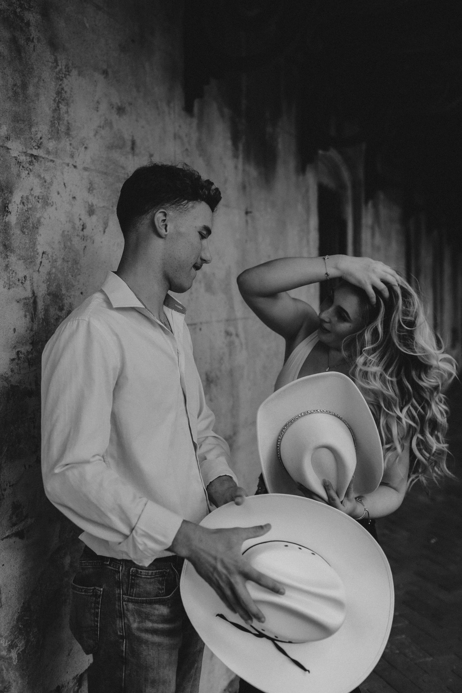 A candid photo of a woman fixing her hair while holding her cowboy hat while her fiance adjusts his hat as well