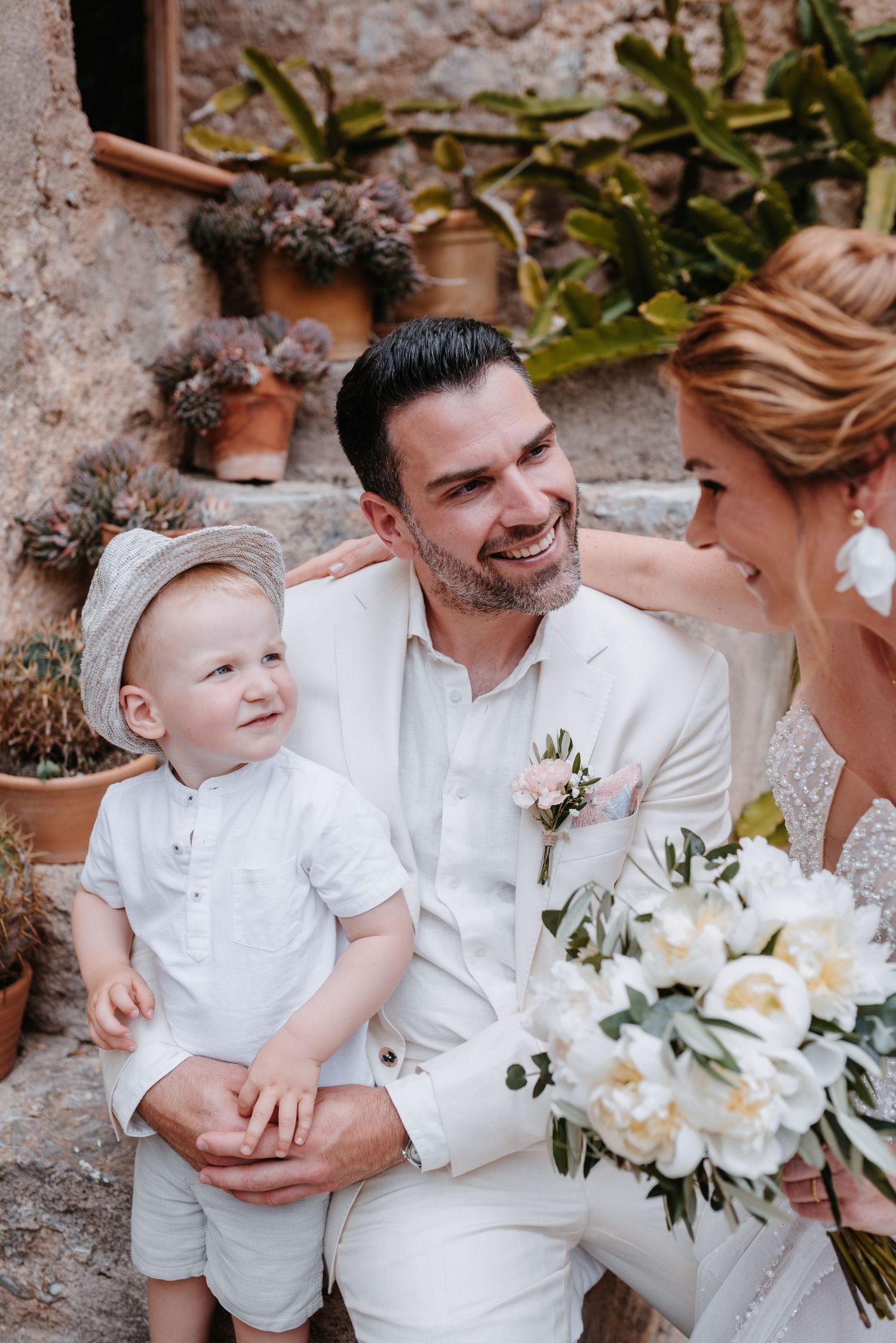 Ein freudiger Hochzeitsmoment, eingefangen in einer eleganten Außenkulisse mit weißen Blumensträußen und passenden weißen Outfits.