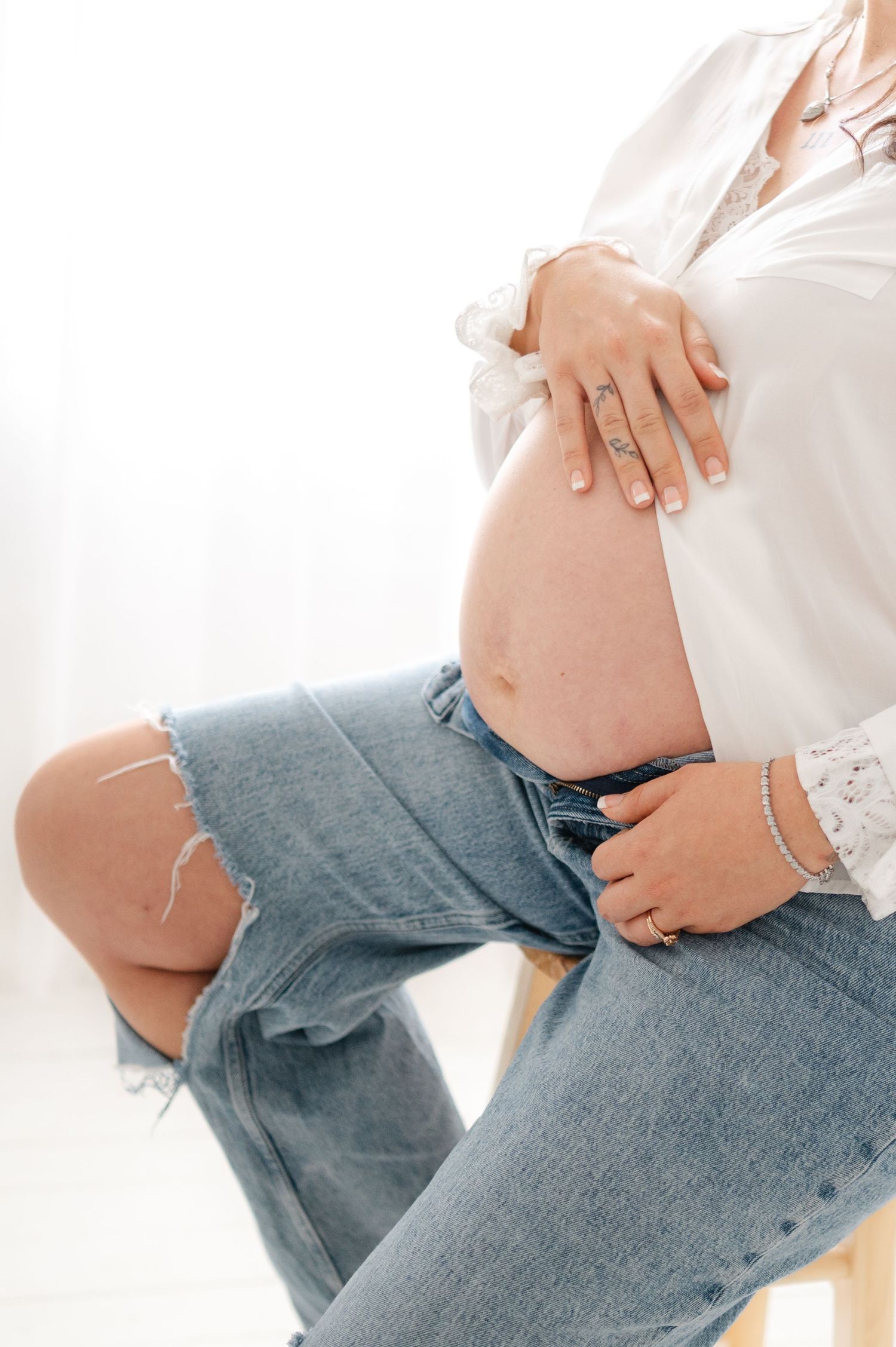 Artistic maternity photos showing a pregnant belly with denim and white shirt styling.