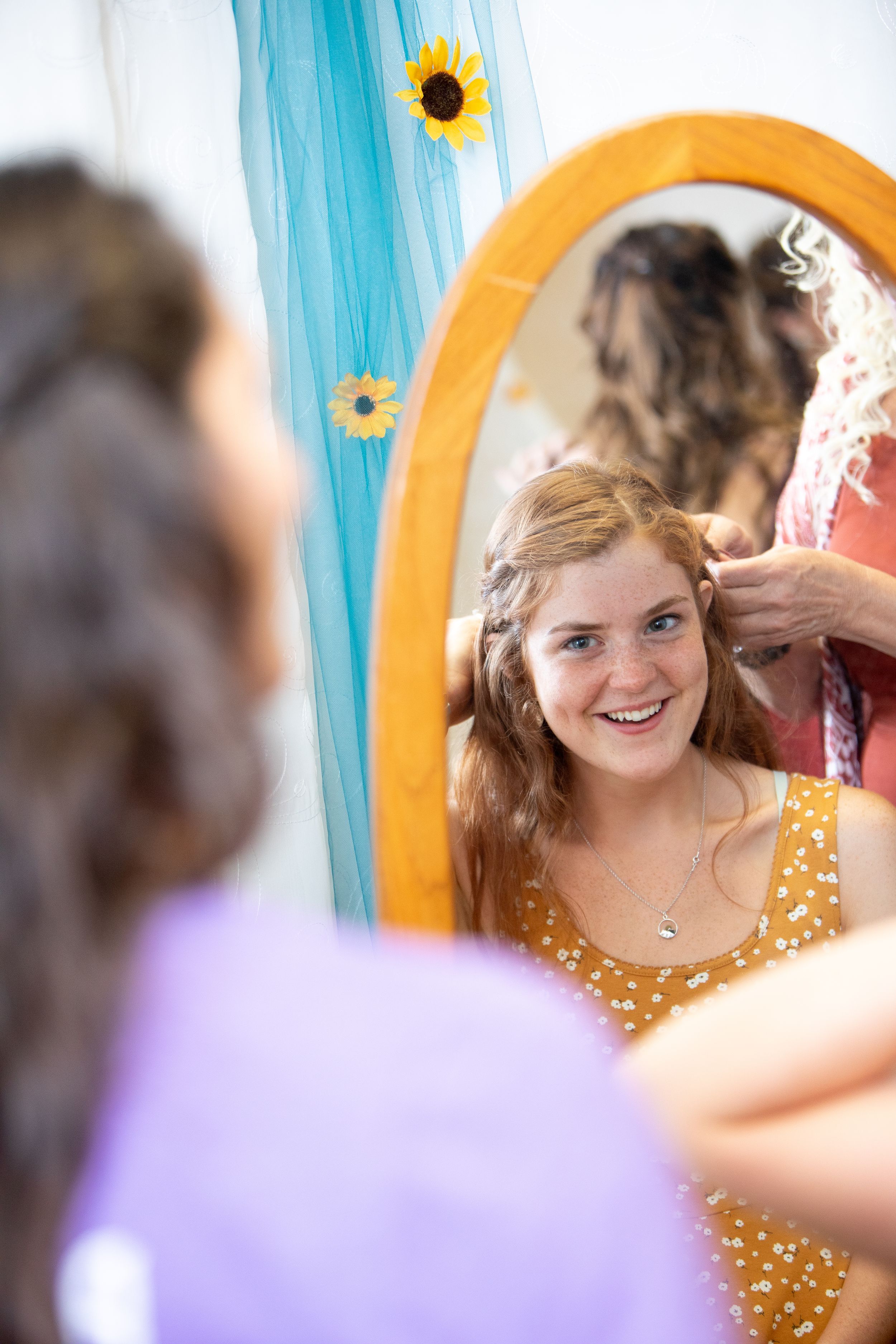 A reflection in an orange-framed mirror shows someone in a polka dot dress getting ready with sunflower decorations nearby.