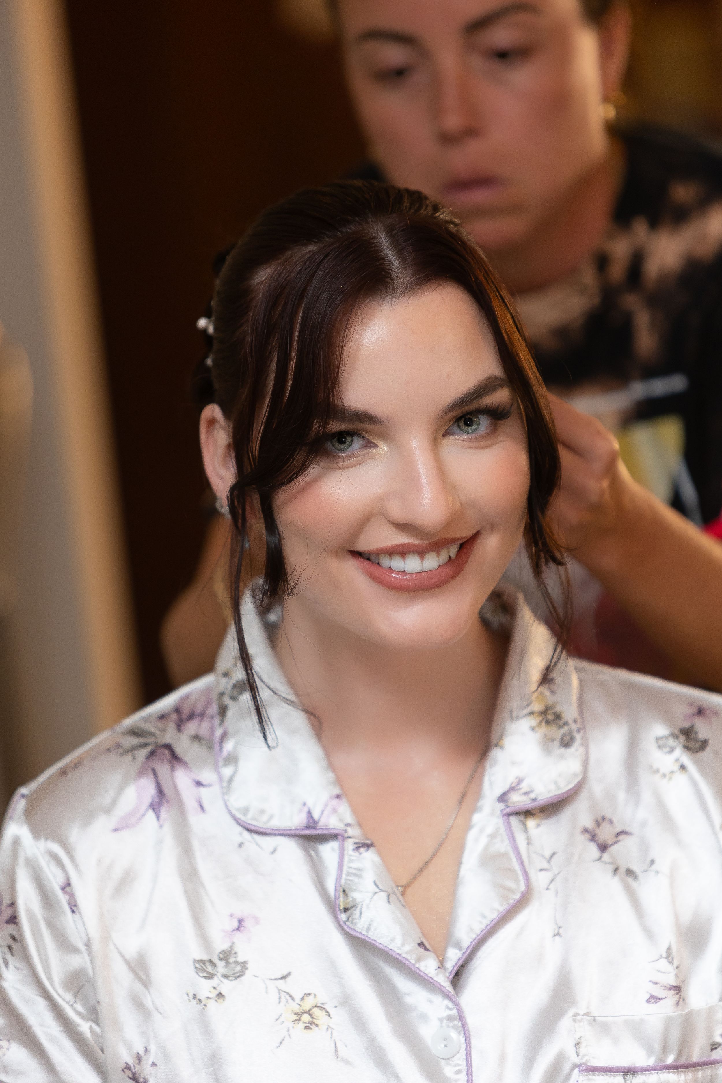 Someone getting their hair styled while wearing a white floral silk robe and smiling at the camera.