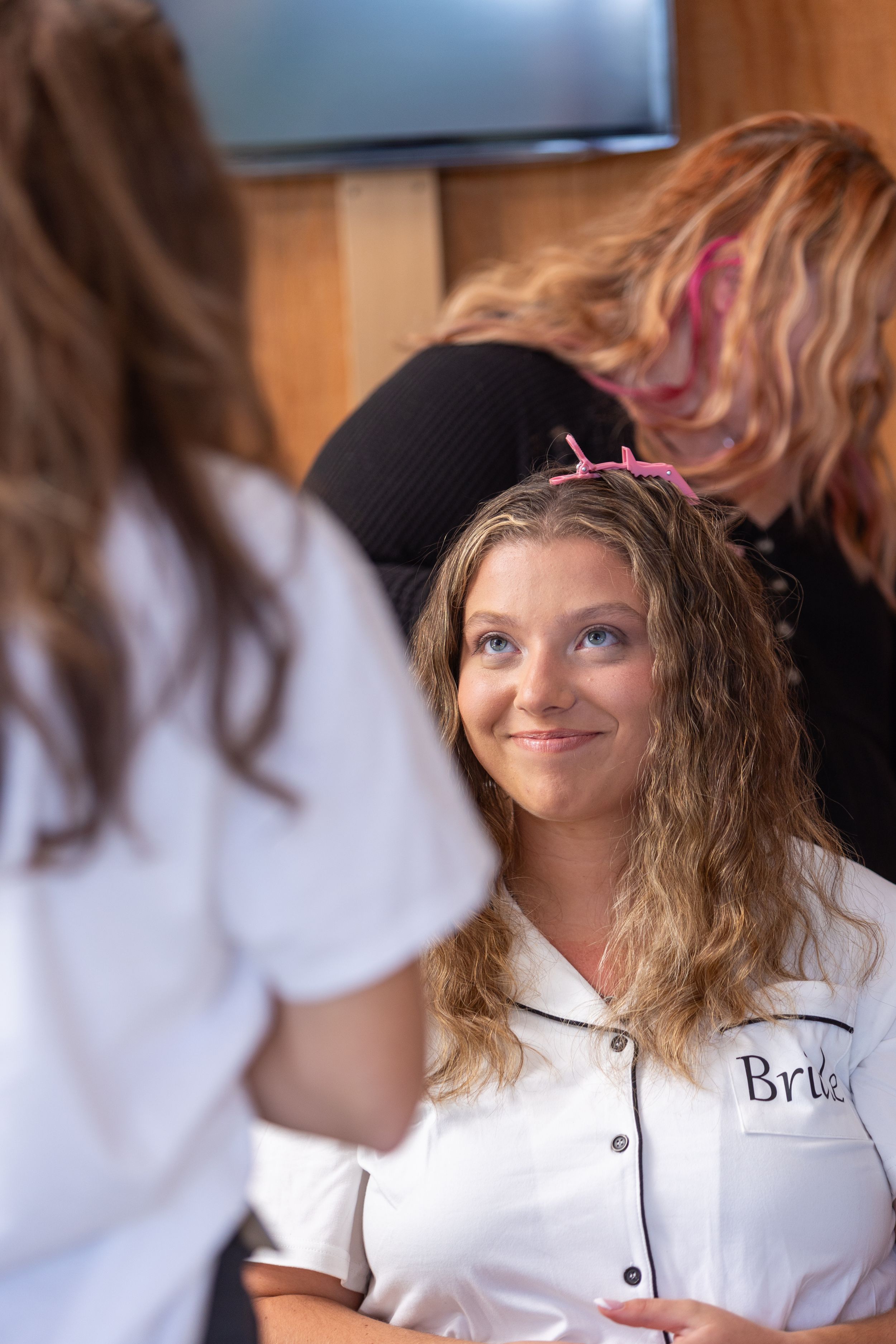 Someone with long wavy blonde hair and pink highlights wearing a white button-up uniform top smiles warmly during a conversation.