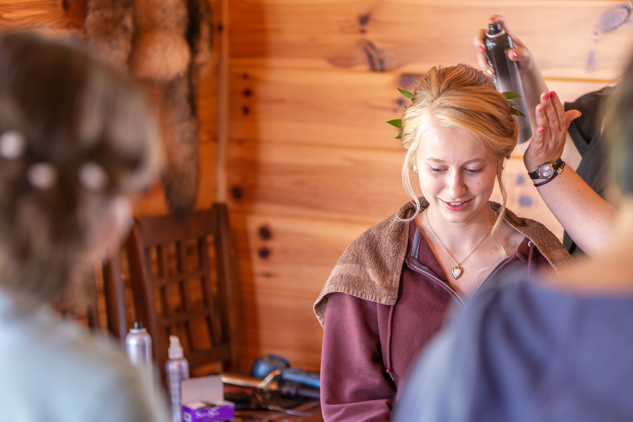 Hair stylist using tools and products while working on a client's hair at a rustic wooden cabin salon.
