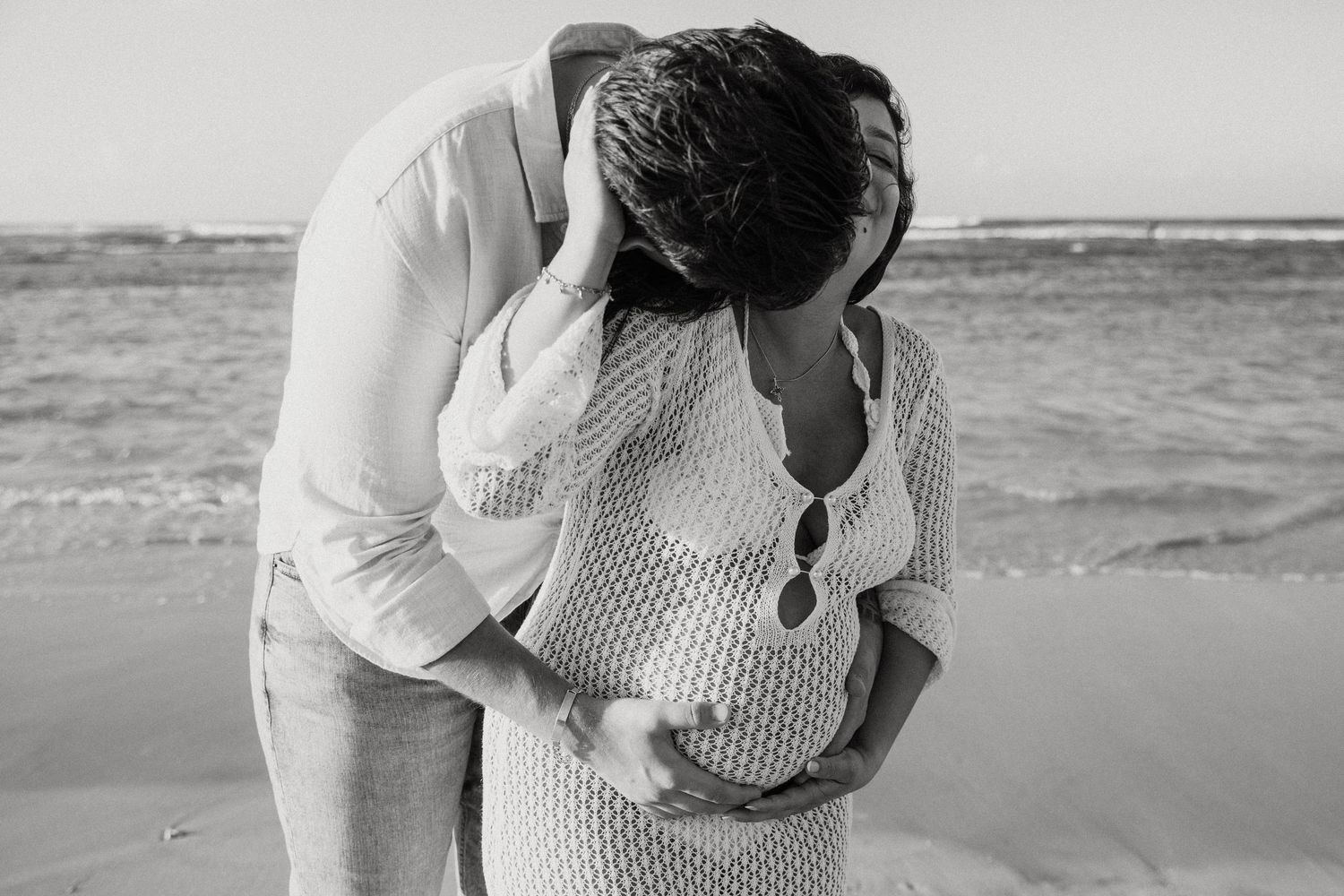 Romantic black and white beach photoshoot capturing couple embracing on sandy shore.