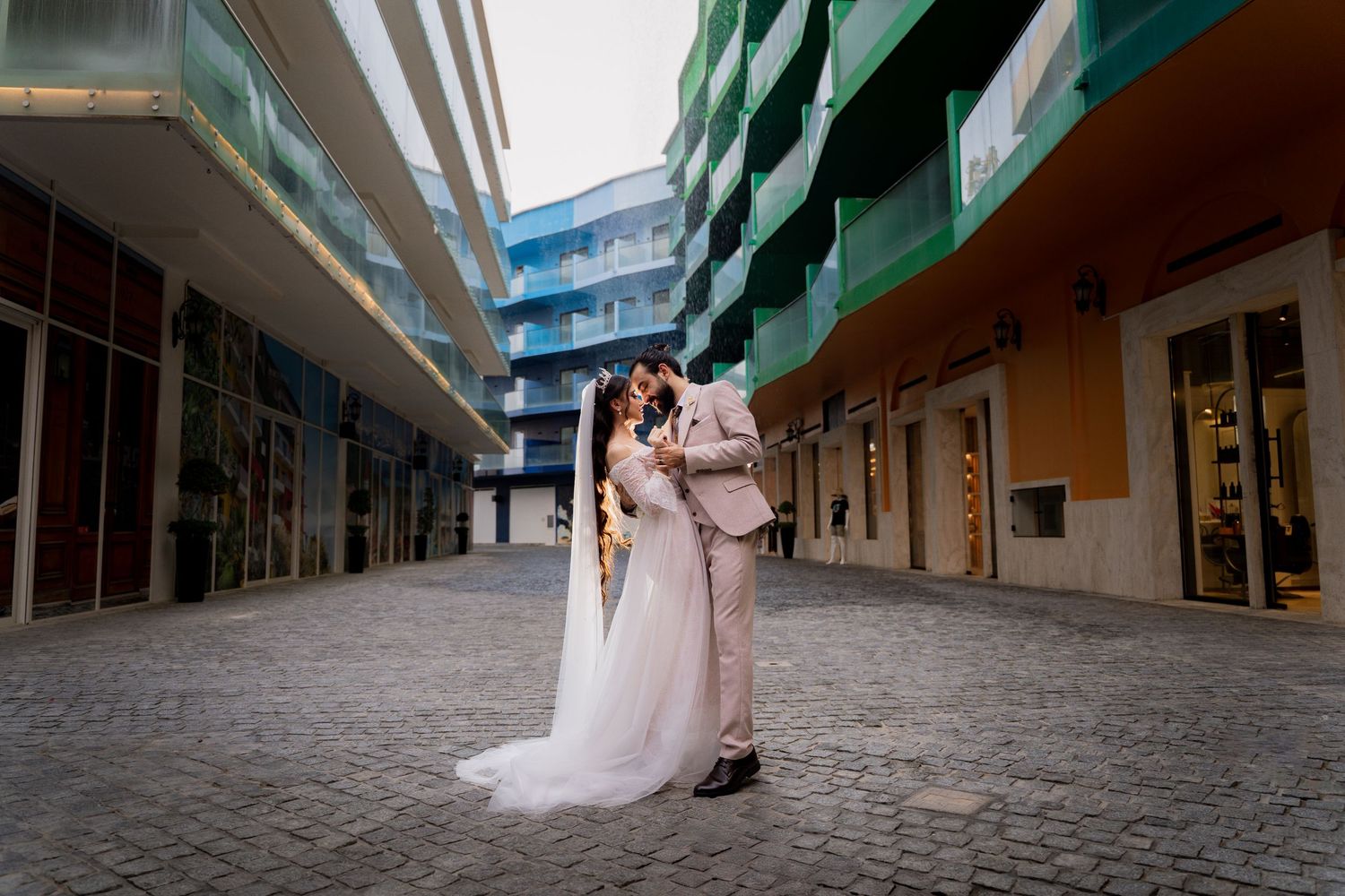 Newlywed couple poses together at a modern architectural venue with colorful overhanging balconies and railings.