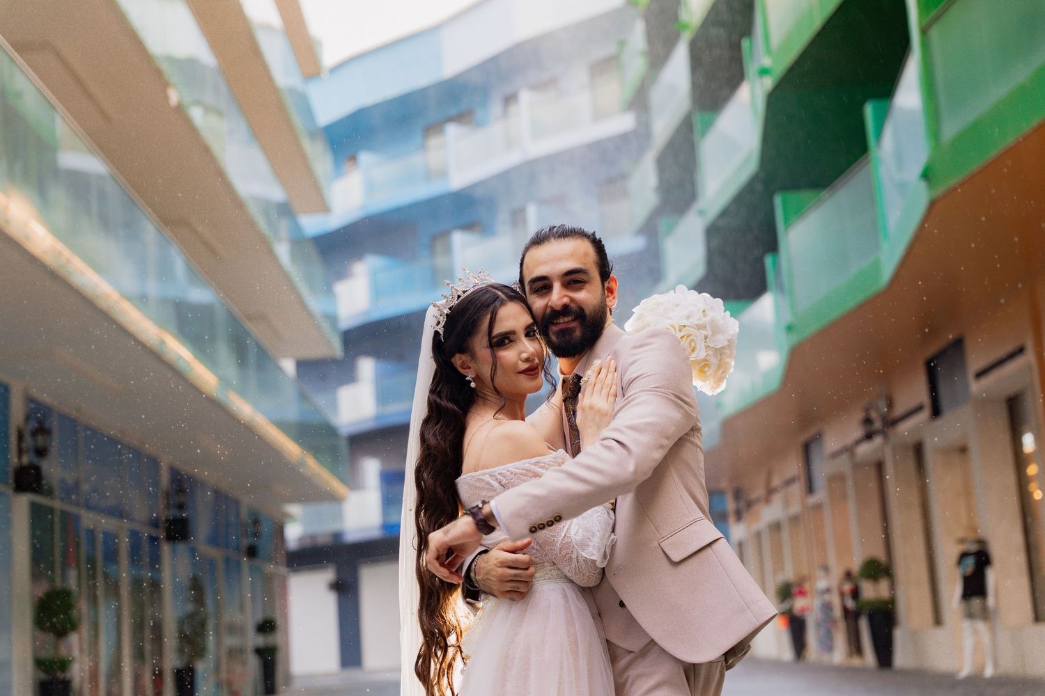 Wedding couple embraces lovingly in outdoor hallway with arched architecture and natural lighting.