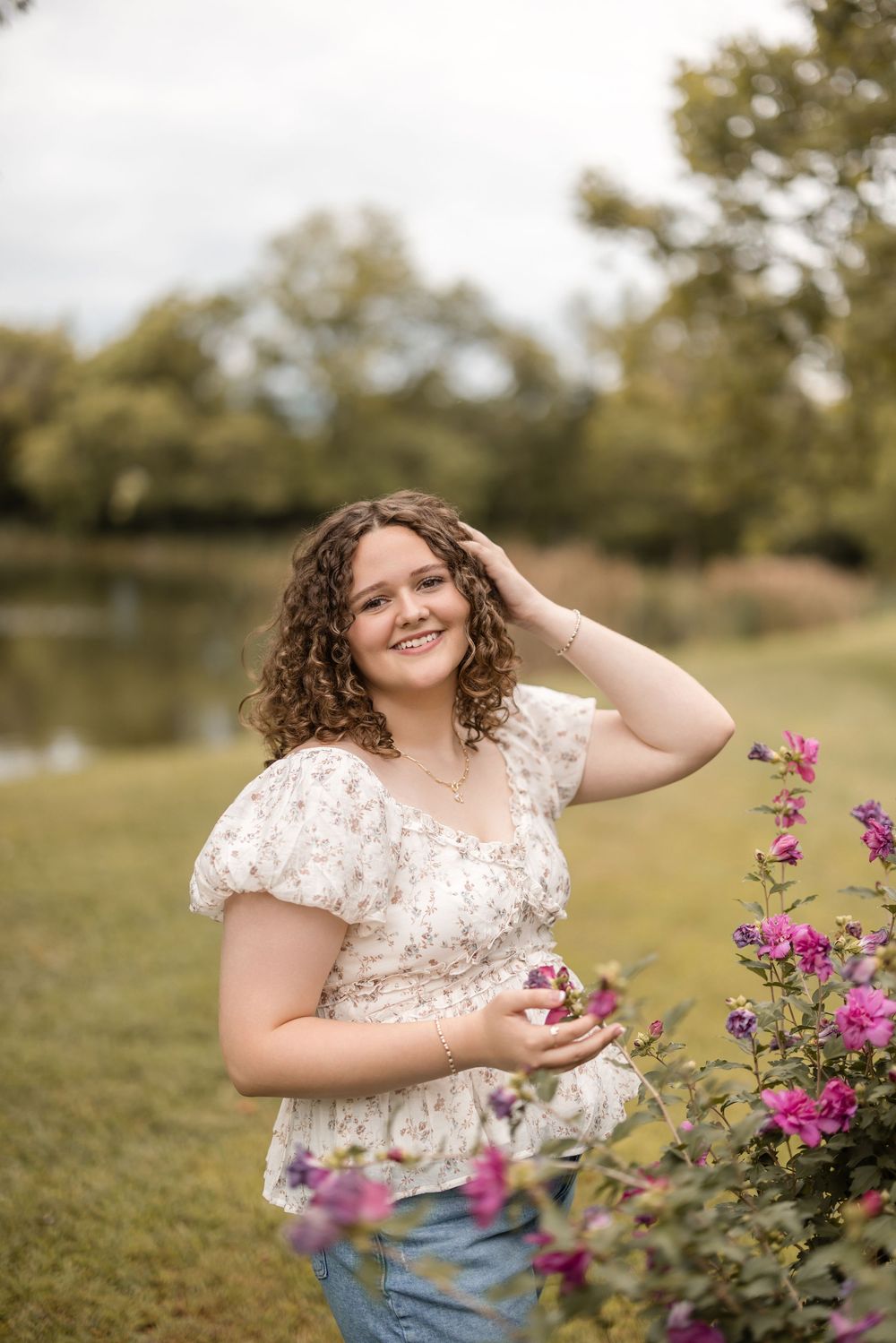 Person in floral dress stands by vibrant pink flowers in a sunny garden setting.