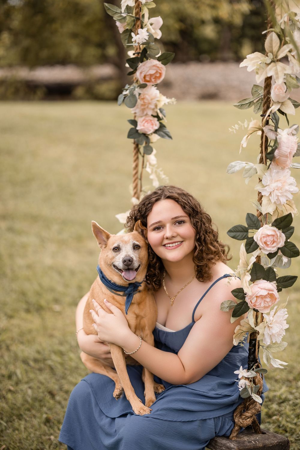 An intimate portrait under a floral-adorned swing featuring a tan dog and someone in a blue dress.