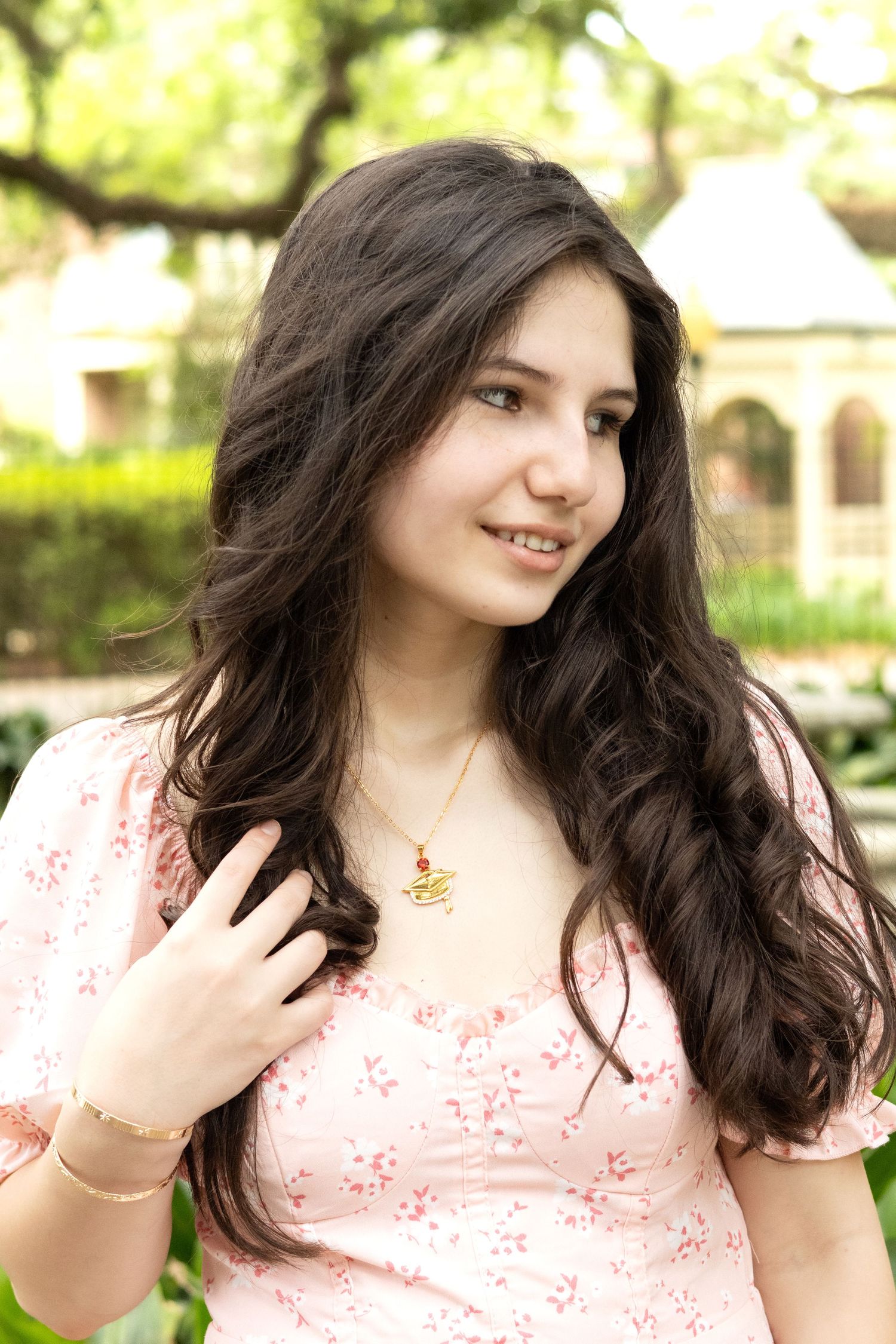 Young woman in pink floral dress poses outdoors in a garden setting.