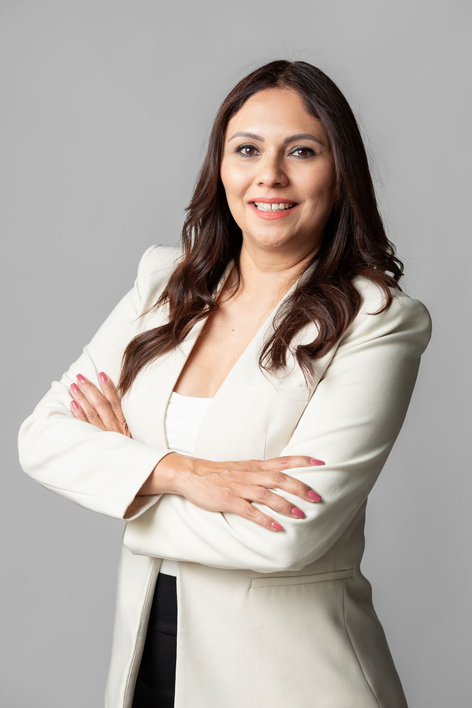 Professional business portrait of person in white blazer and dark hair posing confidently against gray background.