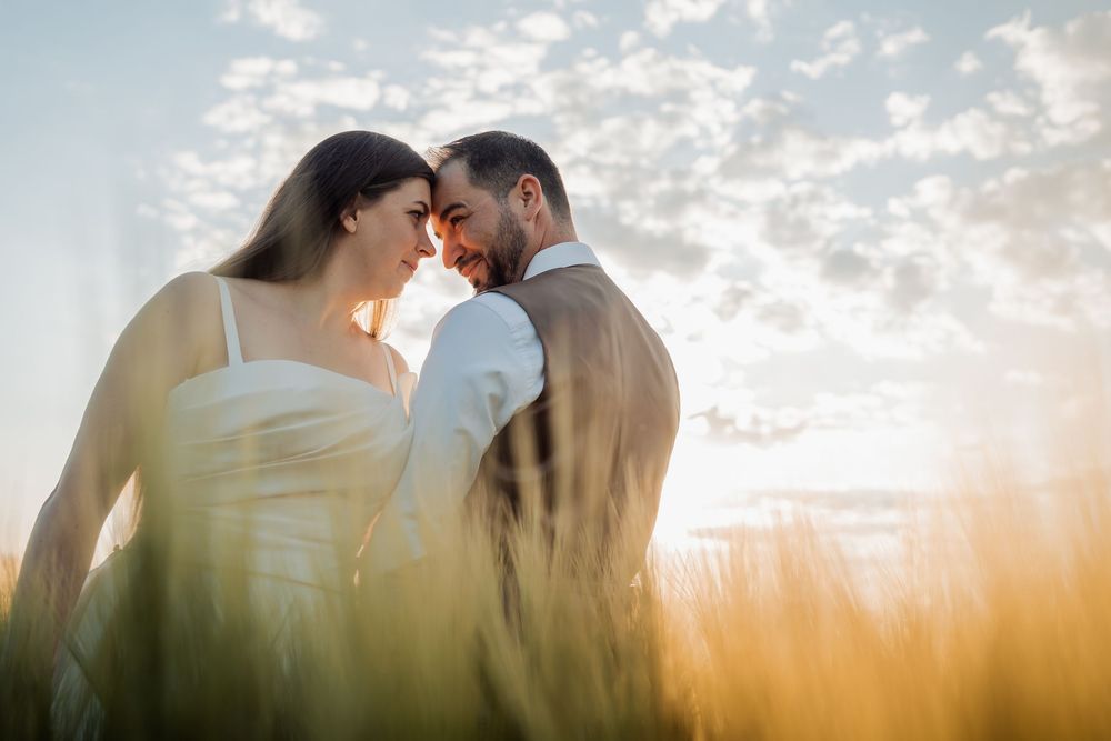 A couple embraces in a sunlit field during golden hour, casting romantic silhouettes against the warm sky.