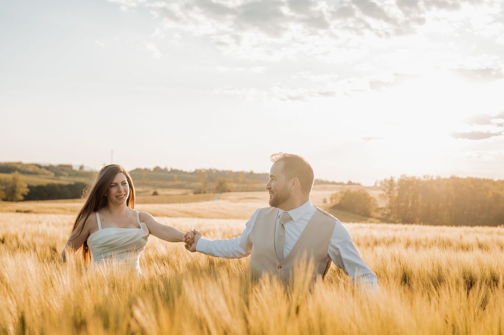 Two people walk hand in hand through a golden wheat field at sunset creating a romantic silhouette against the sky.