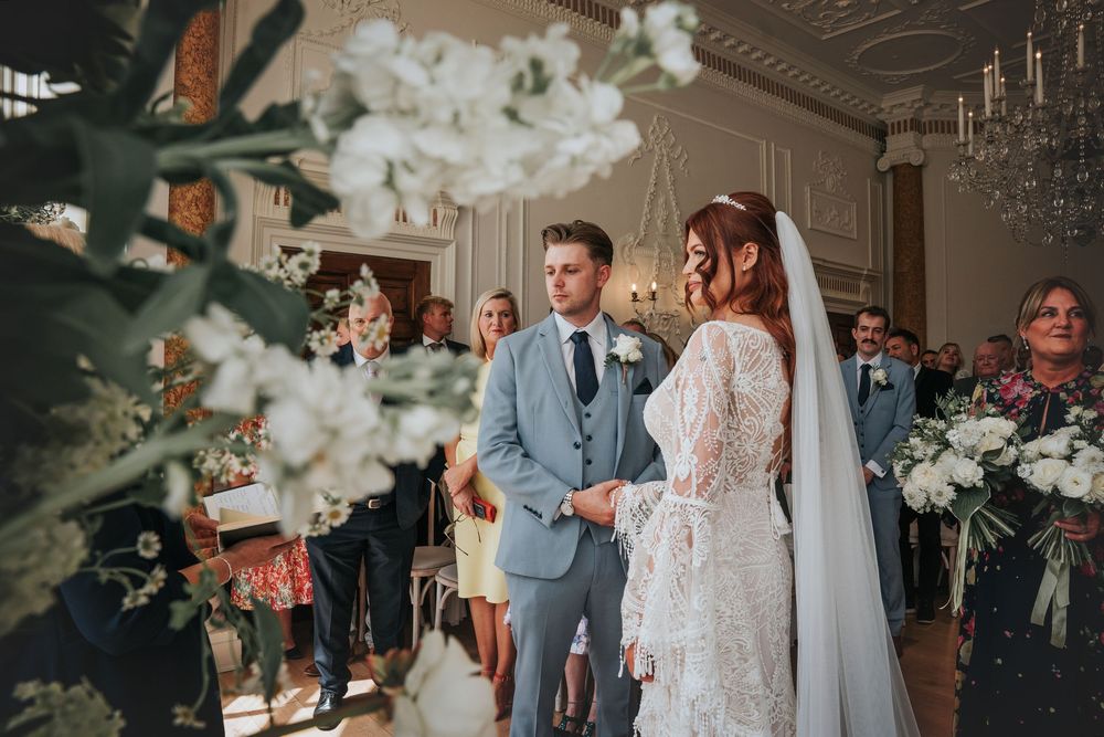 Indoor wedding ceremony at Rockbeare Manor with floral arch around window