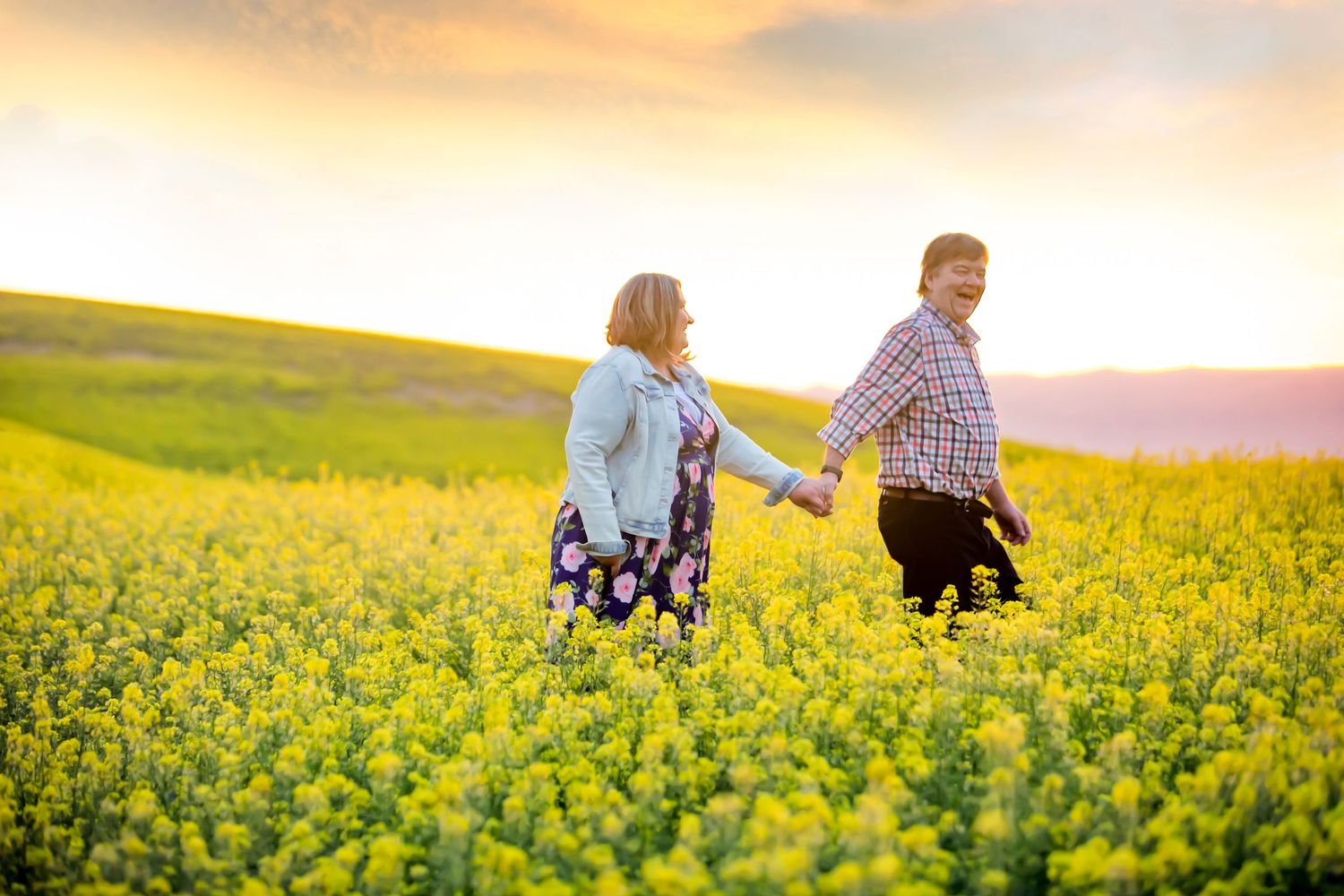 Couple walking through vibrant yellow canola flower field at sunset.