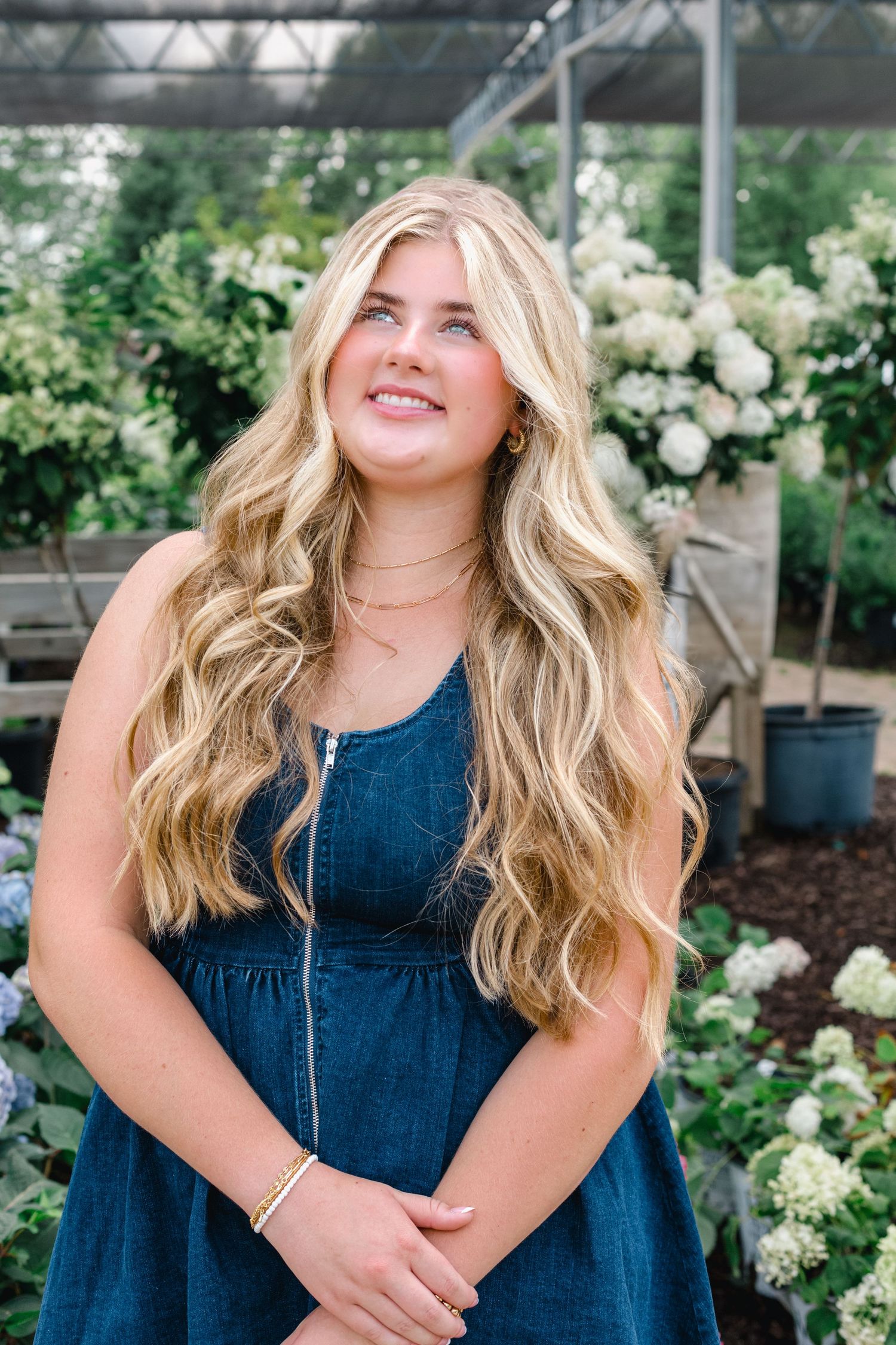 Portrait of someone wearing a denim dress posing against a background of white roses in a garden setting.