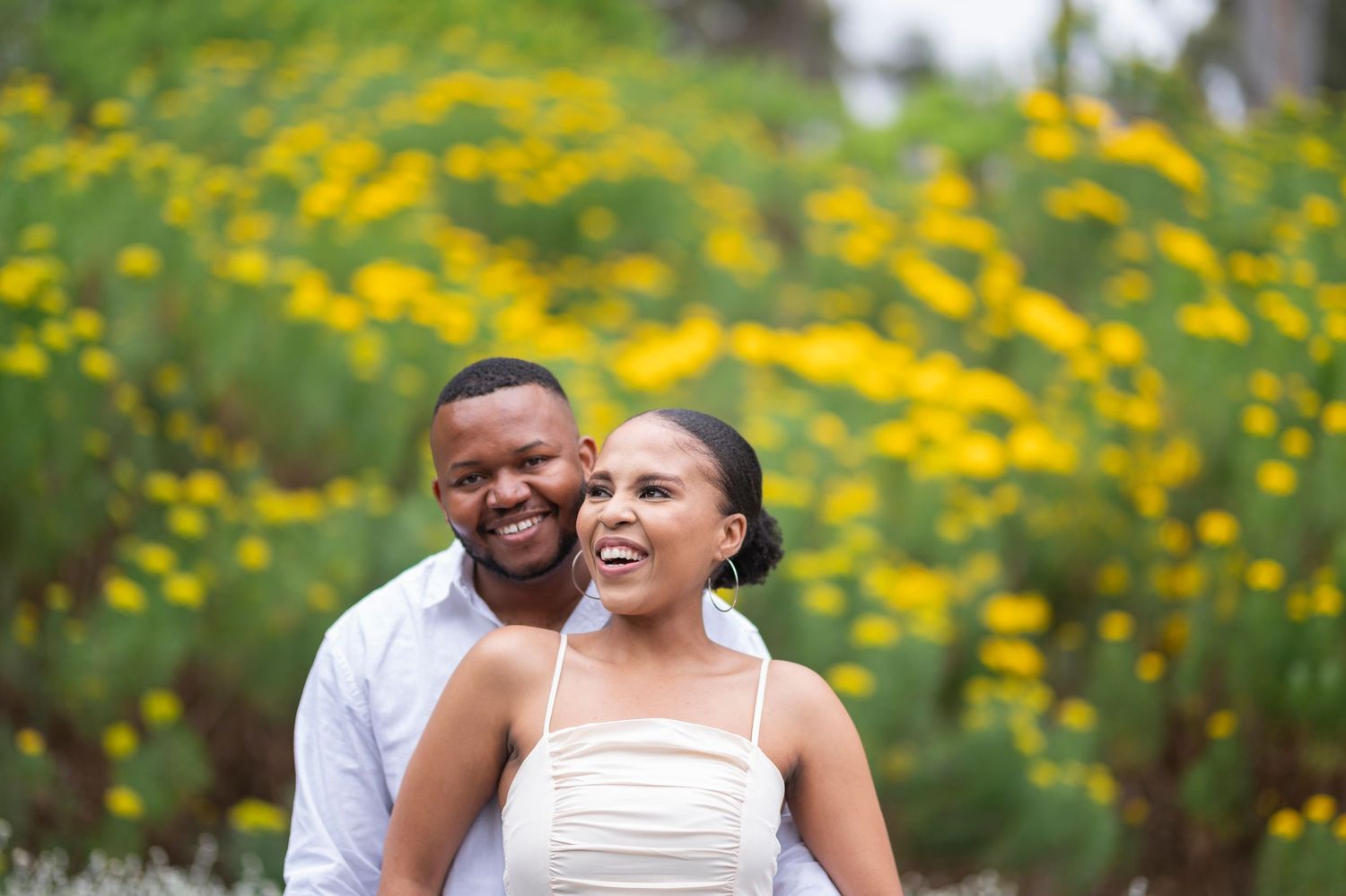 A couple shares joyful moments together in a garden filled with bright yellow wildflowers on a sunny day.