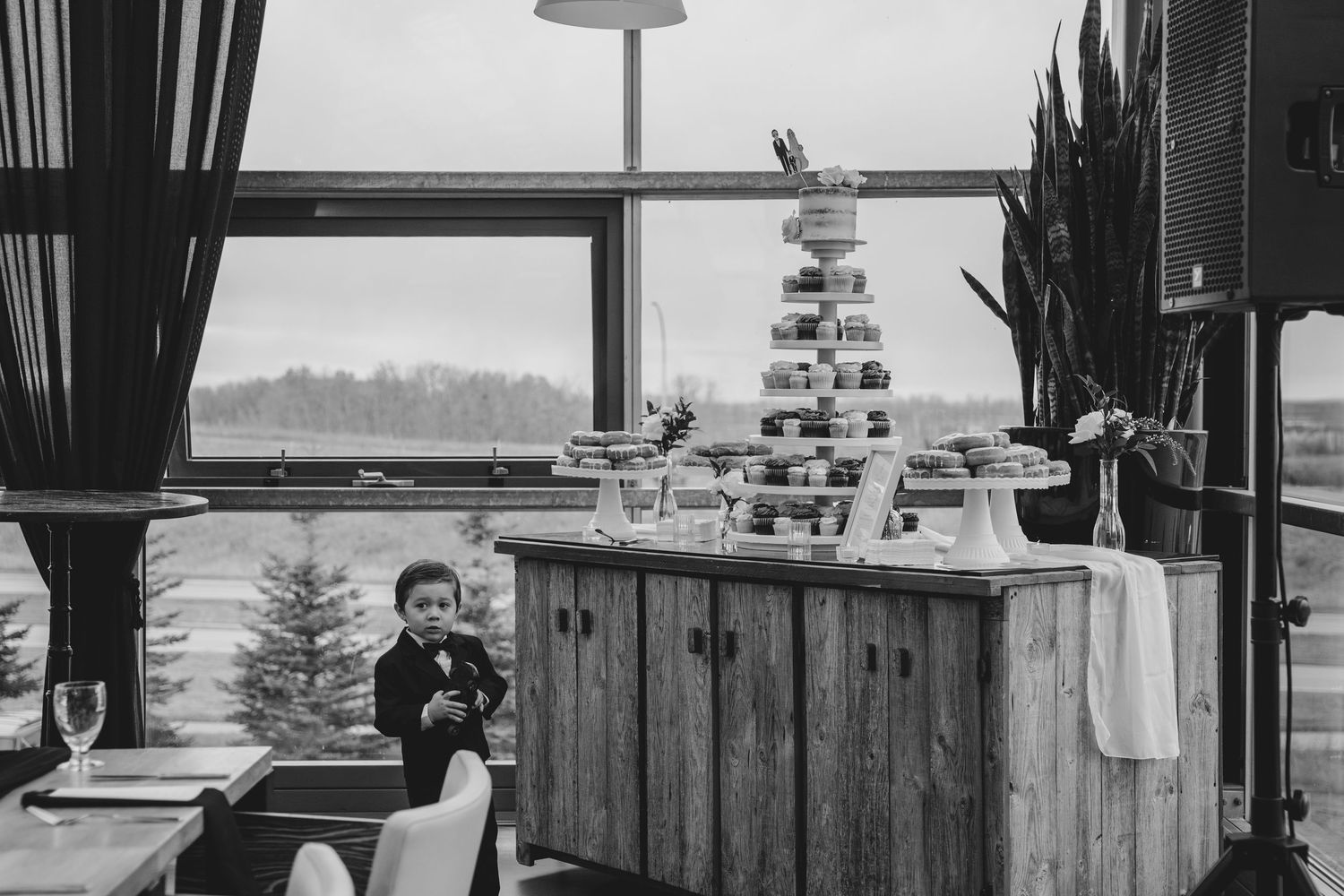Black and white photo of a winter wedding reception with a tiered cake and snowy landscape view through large windows.