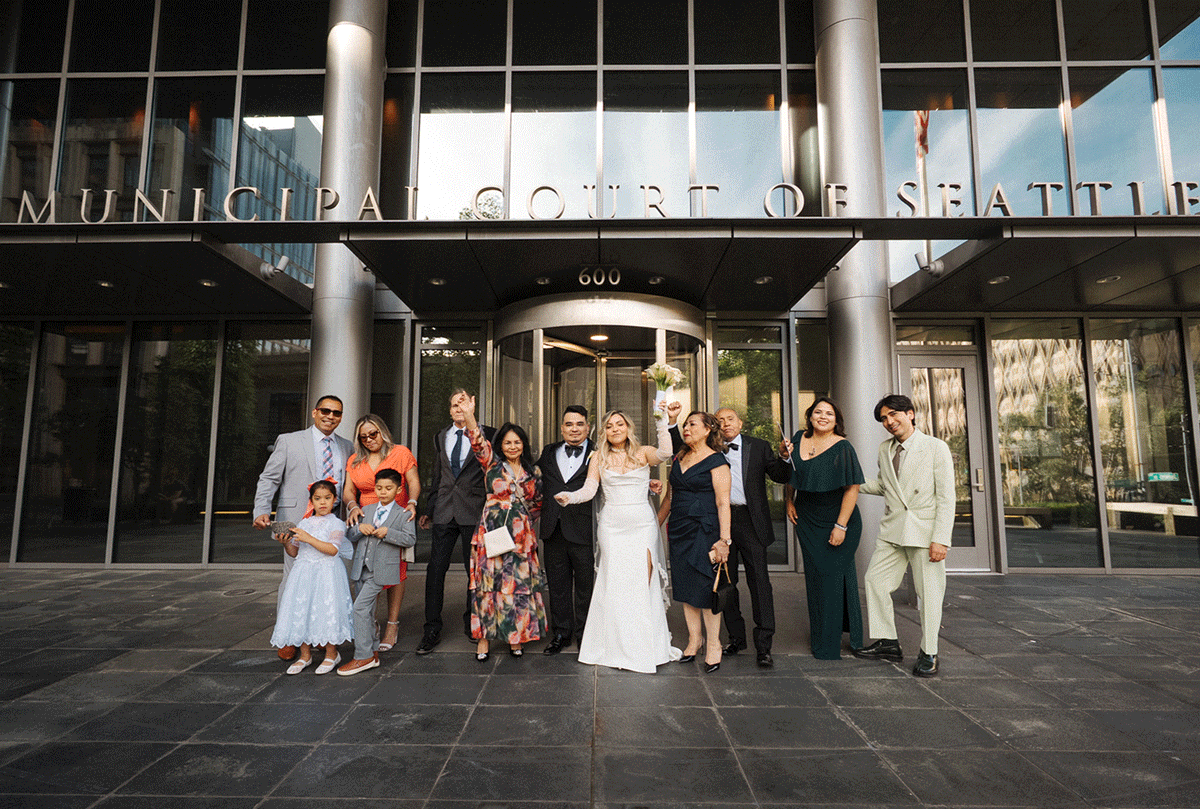 Group stands in front of a concrete and glass building facade for wedding party photos.