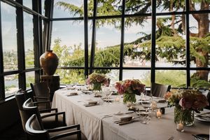 Elegant table settings in an upscale restaurant with panoramic windows overlooking a scenic waterfront view.