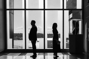 A silhouetted person stands at a window viewing room with floor to ceiling windows overlooking a cityscape.