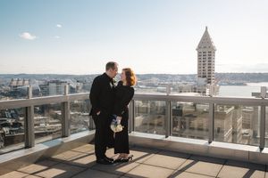 A couple shares a romantic moment on a rooftop terrace overlooking Seattle with Smith Tower visible in the background.