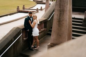 A couple dressed in formal attire embrace on concrete steps, creating an intimate urban setting.