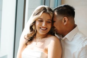 A romantic couple embraces near a bright window, sharing an intimate moment together in natural light.
