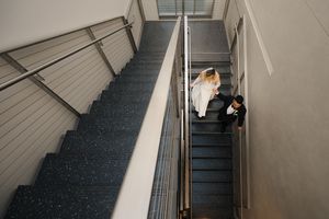 A couple sits together on grey carpeted stairs in an industrial stairwell.