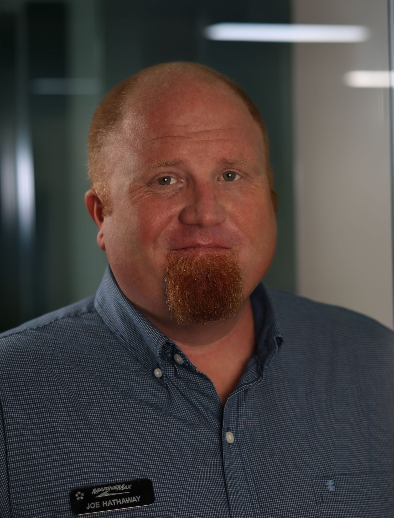 Professional headshot of a person wearing a gray button-up shirt and sporting a reddish beard in an office setting.