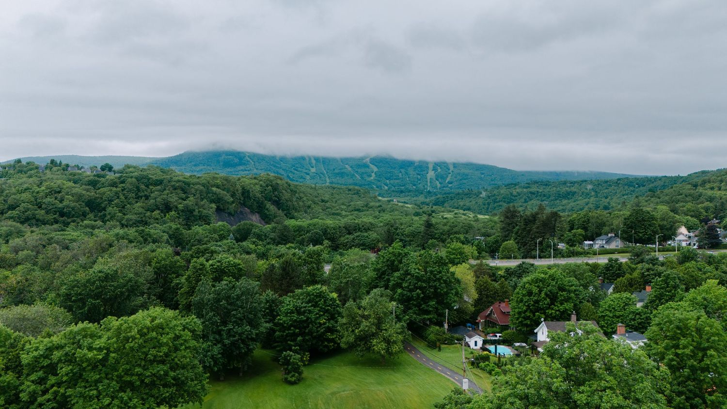 Aerial view of lush green hills and scattered houses in a misty mountain landscape with dense forest.
